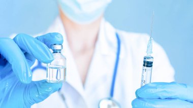 Kadın bir doktor elinde, içinde ilaç ve şırınga olan şeffaf küçük bir şişe tutuyor. Rutin aşılama ve nüfusun aşılanması. Aşı yoluyla sağlığın korunması