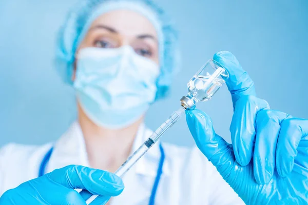 A female doctor holds a syringe and a vaccine in her hands on a blue background. The concept of vaccination and immunization of the population. Vaccination against rubella and human papilloma virus.