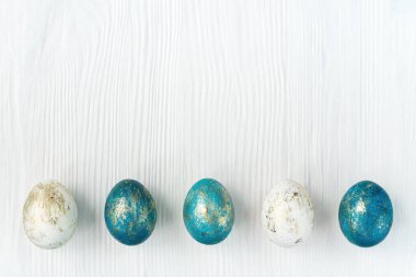 Beyaz ahşap zemin üzerinde mavi ve altın renkli yumurtalar ve fotokopi alanı olan Paskalya tasarım şablonu. Paskalya bayrağı için modern tarzda minimum tasarım. Beyaz arka planda şirin Paskalya yumurtaları.