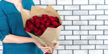 Bir kız kağıt paketinde bir buket kırmızı gül tutuyor. Kız doğum günü, Sevgililer Günü, yıldönümü hediyesi olarak bir buket çiçek aldı. Çiçek teslimat konsepti afişi.