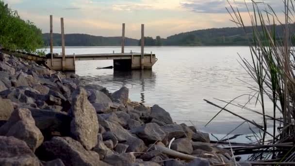 Pier op een bos meer bij zonsondergang. Grote stenen bij het meer Avondlucht boven water — Stockvideo