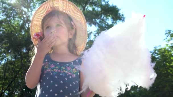 Дівчина їсть бавовняні цукерки в літній сонячний день . — стокове відео
