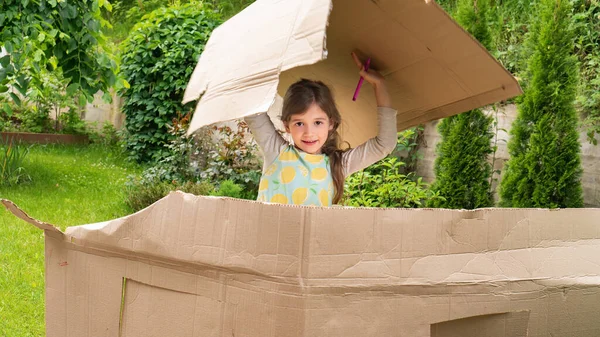The girl plays in the house with a cardboard box. The kid plays in the hostel outdoors. The concept of buying and renting real estate. Tourist accommodation service. Moving to a new home concept.