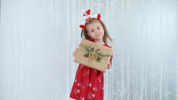 Μικρό χαριτωμένο κορίτσι κρατά ένα vintage τυλιγμένο χριστουγεννιάτικο δώρο σε ένα κόκκινο ρούχα. — Αρχείο Βίντεο