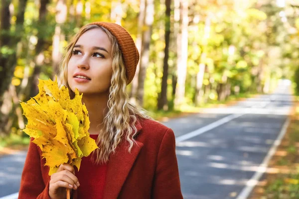 Uma menina bonita em roupas quentes, segurando ltsya amarelo em suas mãos, fica na natureza no outono. O conceito de recreação e passatempo — Fotografia de Stock