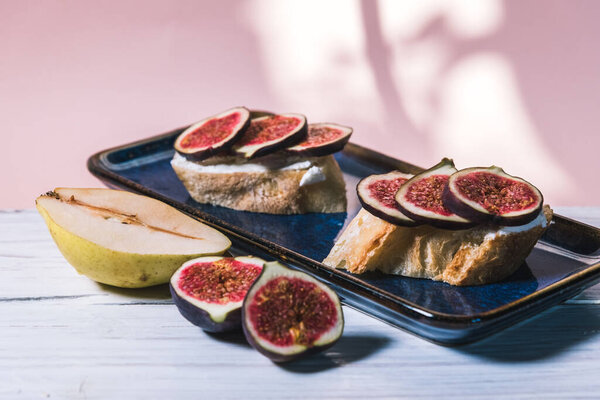 Bruschetta of baguette, cheese and figs are on a plate on the table. The concept of minimalism in food
