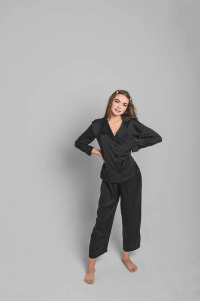 Una hermosa mujer con el pelo largo y el maquillaje en pijamas con estilo se encuentra sobre un fondo gris en el estudio. Concepto de tiro de moda — Foto de Stock