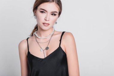 Uzun saçlı, uzun gecelikli, makyajlı ve takılı güzel bir kadın stüdyoda gri bir arka planda duruyor. Moda çekim konsepti