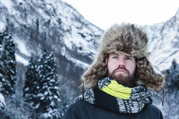 한 성인 잔인 한 남자가 스카프를 두르고 모자를 쓰고 겨울에 산에 서 있습니다. 적극적 인 여가 활동 개념 스톡 사진