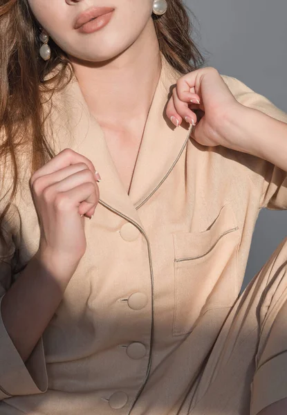 Eine schöne Frau mit langen Haaren und Make-up in stylischem Pyjama sitzt auf beigem Hintergrund im Studio. Konzept für Modeschießen — Stockfoto