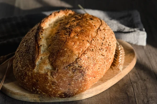 Ręcznie robiony tartinowy chleb leży na drewnianej powierzchni obok kłosów pszenicy. Koncepcja produkcji rolnej i pieczenia w domu — Zdjęcie stockowe