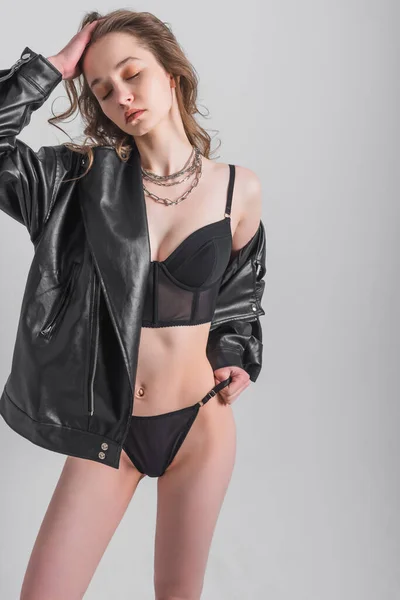 A woman with dyed hair and make-up in underwear and a jacket stands in the studio on a gray background. Fashion shooting concept
