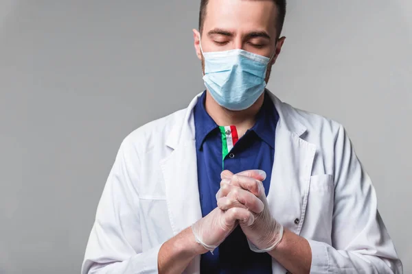 Молодой человек в медицинской одежде в маске и перчатках стоит на сером фоне в студии. Здравоохранение и медицинское обслуживание — стоковое фото