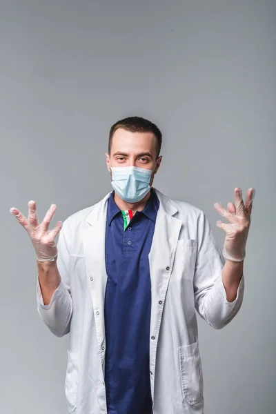 Un jeune homme en tenue médicale portant un masque et des gants se tient sur un fond gris dans le studio. Concept de soins de santé et de services médicaux — Photo