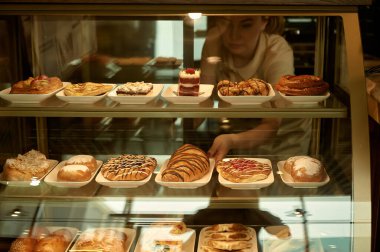 Bir garson bir pastanede müşteriye hizmet eder. Bir kadın kahvaltı için kek ve kurabiye alır.. 