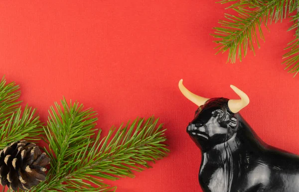 Estatueta de um touro em um fundo vermelho de Natal. foco seletivo. decorações festivas e ramos de abeto com cones. — Fotografia de Stock
