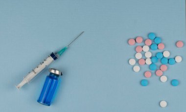 Tıbbi şırınga ve mavi arka planda renkli haplar. Aşılama ve tedavi arasında seçim yapın.