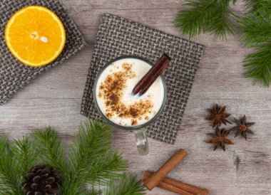 Geleneksel bayram içkisi. Çiğ tavuk yumurtası ve süte dayalı tatlı bir içecek. Rendelenmiş hindistan cevizi ve tarçınlı Noel kokteyli. Külahlı bir ladin dalının arka planı. Üst görünüm, boşluk kopyala.