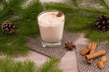 Geleneksel bayram içkisi. Çiğ tavuk yumurtası ve süte dayalı tatlı bir içecek. Rendelenmiş hindistan cevizi ve tarçınlı Noel kokteyli. Külahlı bir ladin dalının arka planı. xmas iç..