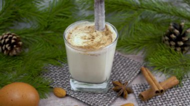 Geleneksel bayram içkisi. Çiğ tavuk yumurtası ve süte dayalı tatlı bir içecek. Rendelenmiş hindistan cevizi ve tarçınlı Noel kokteyli. Külahlı bir ladin dalının arka planı. xmas iç..
