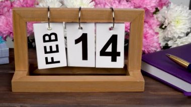 14 Şubat tarihli masaüstü takvimi ve bir buket güzel çiçek. Sevgililer Günü için narin kasımpatılar. Ay ve gün içinde el yapımı ahşap küp. Gün için planlama.