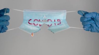 Covid-19 ateşle yanıyor. Cerrahi maskeyi ateşe vermek, solunum cihazlarını yok etmek. Koronavirüs salgınının sonu. Koruyucu yüz maskesinin yakılması. 