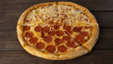 Ahşap arka planda lezzetli bir pizza. Peperoni ve Hawai 'li, iki parçalı pizza. Maya hamurundan yapılmış ince yuvarlak tortilla şeklinde geleneksel İtalyan yemeği. fast food