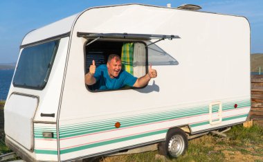 Adam bir seyahat karavanıyla rahatlıyor. Karavan, yolcuların konforunu sağlamak için gerekli tüm ev aletleriyle donatılmıştır. Karavan, karavan karavanı. yaz tatili konsepti