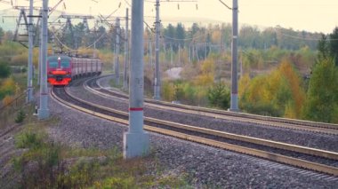 Rusya, Krasnoyarsk, Eylül 2021: Bir sonbahar ormanının arka planında demiryolunda elektrikli tren yolculuğu. Rus demiryollarının lokomotifi.