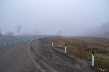 Görüş mesafesi düşük bir yol. Pistte sonbahar yapraklarının arka planına karşı sis var. Seçici odak ve ışık bulanıklığı.