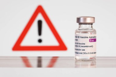Montreal, CA - 15 March 2021: Vial of Astrazeneca Covid-19 vaccine in front of a danger sign clipart