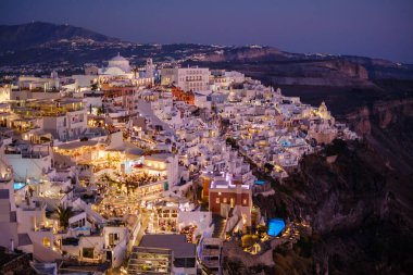 Santorini, GR - 4 Eylül 2025: İkonik beyazlatılmış binaları, dramatik uçurumları ve alacakaranlıkta parlayan şehir ışıklarıyla aydınlatılan Ege Denizi ile Fira şehir manzarasını görüntüler