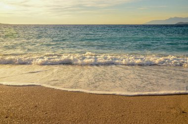 Kumlu sahilde deniz dalgaları ve köpük, gün batımı gökyüzü 