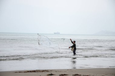 Sahildeki tanımlanamayan adam balık yakalamak için ağ atıyor.