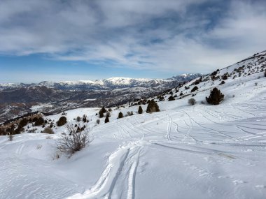 Beyaz karda kayak pisti dağ yamacından aşağı iniyor. Mavi gökyüzü ile kış dağı manzarası. Açık hava kış sporu ve macera konsepti.