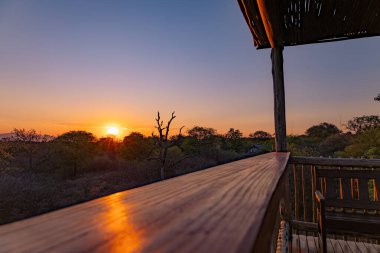 Özel ahşap bir kulübe verandasından görünen savana manzarasının üzerinde güzel bir günbatımı. Afrika vahşi yaşam manzarası, safari tatili, turizm ve seyahat konsepti.