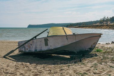 Denizin yanındaki kumlu sahilde kürekli eski bir balıkçı teknesi. Açık mavi gökyüzü yalnızlığı ve huzuru temsil ediyor.