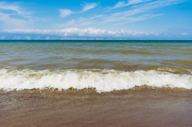 Ocean beach wave arriving on a sand shore under blue sky. Nature outdoor landscape for summer background or travel concept.