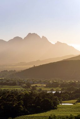 Gün batımında dağ manzarası, köy, üzüm bağı ve göl. Seyahat ve turizm için altın saatinde cennet manzarası