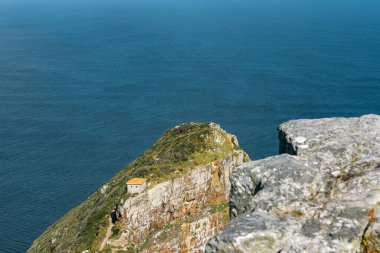Güney Afrika, Ümit Burnu 'ndaki engin mavi okyanusa bakan bir uçurumun kenarına kurulmuş küçük bir taş bina. Seyahat ve doğa için ideal deniz manzarası.