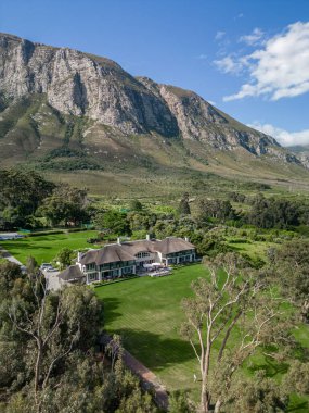 Görkemli bir dağın eteklerinde sazdan bir çatısı olan, yeşil çimenler ve ağaçlarla çevrili, lüks gayrimenkul reklamları için büyük bir malikane evi..