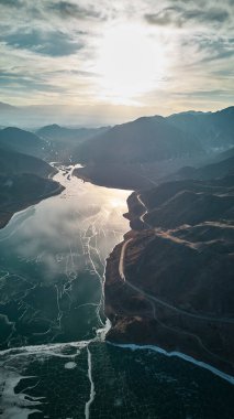 Gün batımında dağ manzaralı donmuş bir göl manzarası görkemli bir doğal zemin oluşturuyor. Yolculuk için güzel bir kış manzarası.