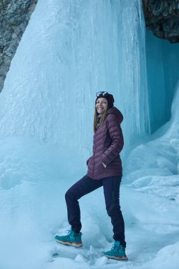 Donmuş bir şelaleyi keşfeden kadın turist, doğal bir buz oluşumu. Açık hava ve doğa fotoğrafçılığı için kış yolculuğu macera konsepti.