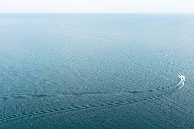Okyanus yüzeyinde iz bırakan bir sürat teknesinin havadan görünüşü. Deniz macerası ve mavi suyla yaz tatili konsepti.