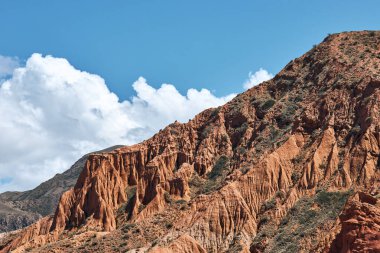 Kırgızistan 'daki kırmızı kaya dağı mavi gökyüzü ve beyaz kümülüs bulutlarıyla. Tien Shan manzara, seyahat günlüğü, kartpostal.