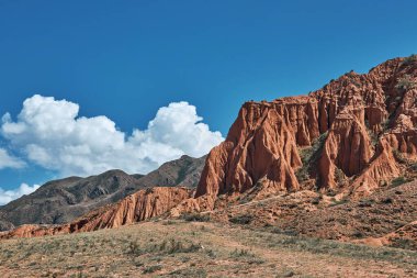 Kırgızistan 'ın Tien Shan dağlarında kırmızı kil kaya oluşumu. Gezmek için mavi gökyüzü olan canlı kanyonun güzel panoramik manzarası.