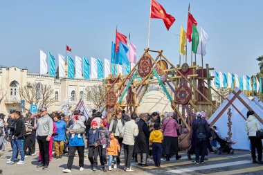 Kırgızistan, Bişkek 'te Nooruz' u kutlayan geleneksel çadır ve bayrakların önünde yürüyen insanlar. Kültür festivali ve bahar tatili. Bishkek, Kırgızistan - 21 MAR 2023.