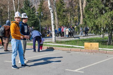 Geleneksel Ak Kalpak başlıklı iki Kırgız, Nooruz festivali sırasında bir Alchik oyun tahtasının yanında duruyor. Bishkek, Kırgızistan - 21 MAR 2023.