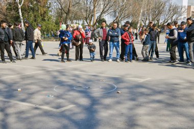 Erkekler ve kadınlar parayla Alchiki oynayan insanları izliyorlar. Nooruz festivalinde aile. Geleneksel Kırgız kültürünün kutlanması. Bishkek, Kırgızistan - 21 MAR 2023.