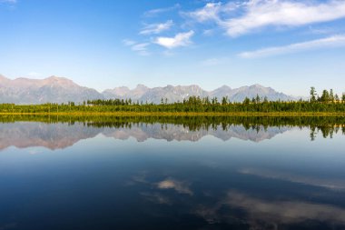 Dağ sırası sakin göle yansıyor. Seyahat, turizm ve açık hava eğlencesi için açık mavi gökyüzü olan güzel doğal manzara..